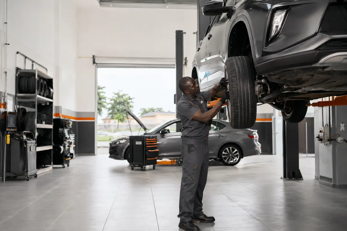 Technicien Nabaya remontant une roue sur un véhicule levé dans l'atelier de Conakry